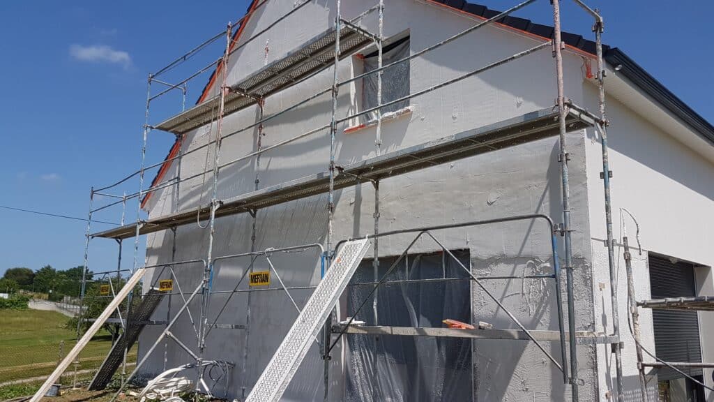 Rénovation de façade et enduit avec échafaudage MEFRAN Maison blanche en cours d'enduisage avec échafaudage MEFRAN sur un chantier de construction.